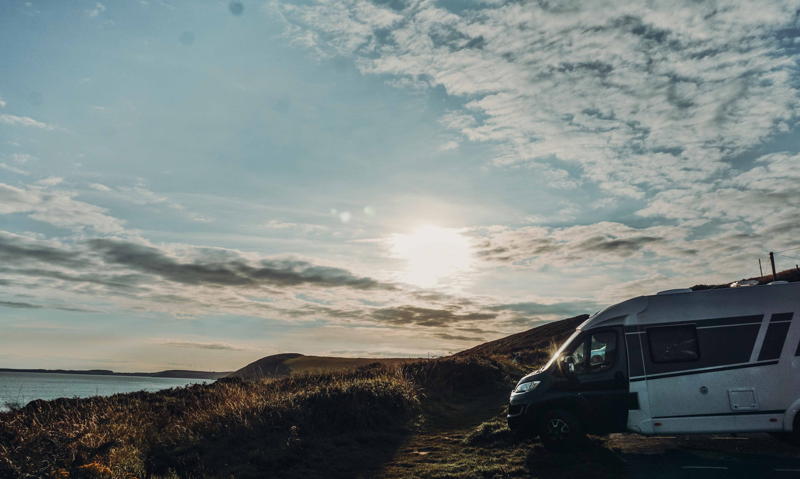 Asuntoauto pysäköity rannikkomaisemaan auringonlaskun aikaan, näkymä merelle